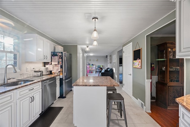 kitchen featuring stone counters, a breakfast bar, appliances with stainless steel finishes, a sink, and a kitchen island