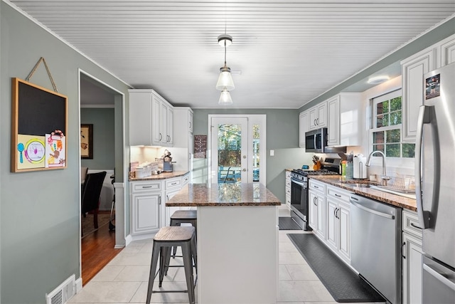 kitchen with a center island, stainless steel appliances, visible vents, a sink, and dark stone counters