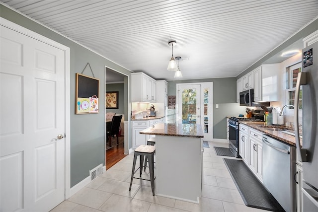 kitchen with stainless steel appliances, a kitchen island, a sink, visible vents, and dark stone countertops