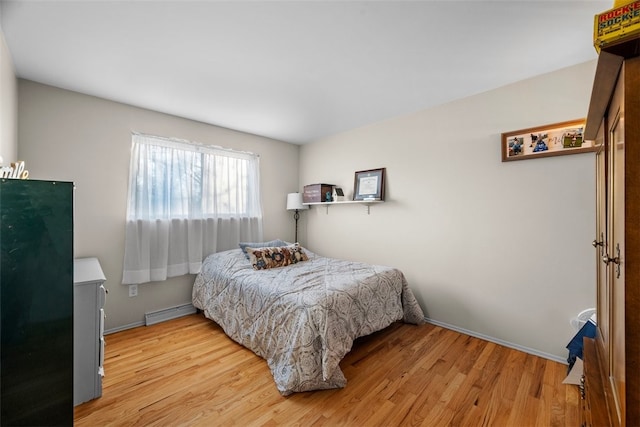 bedroom with a baseboard heating unit, light wood finished floors, and freestanding refrigerator