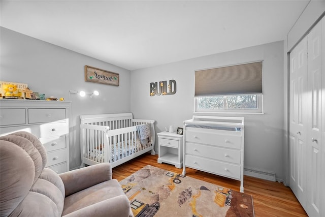 bedroom with a nursery area, a closet, and wood finished floors