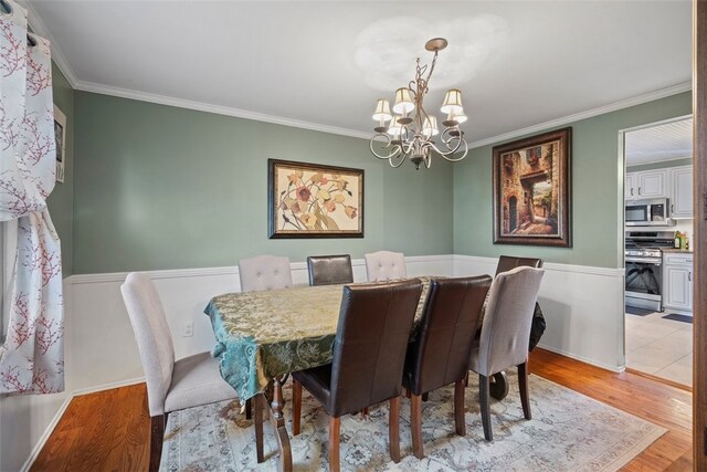 dining space with ornamental molding, light wood-type flooring, and an inviting chandelier