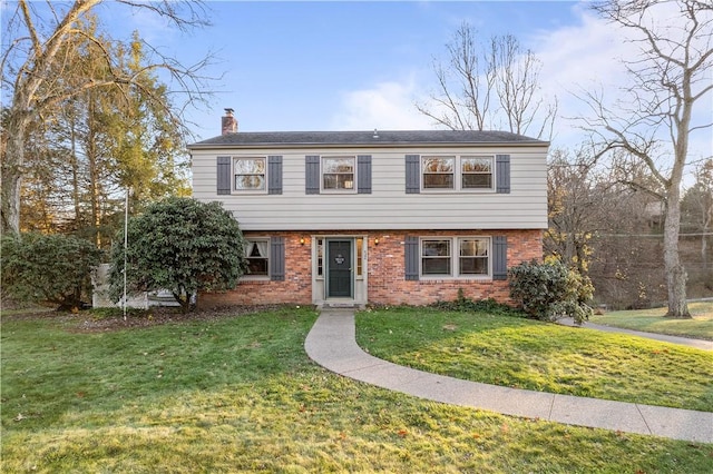 colonial house with brick siding, a chimney, and a front lawn