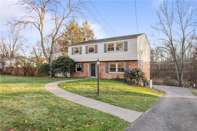 colonial-style house with a front yard, a chimney, aphalt driveway, and brick siding