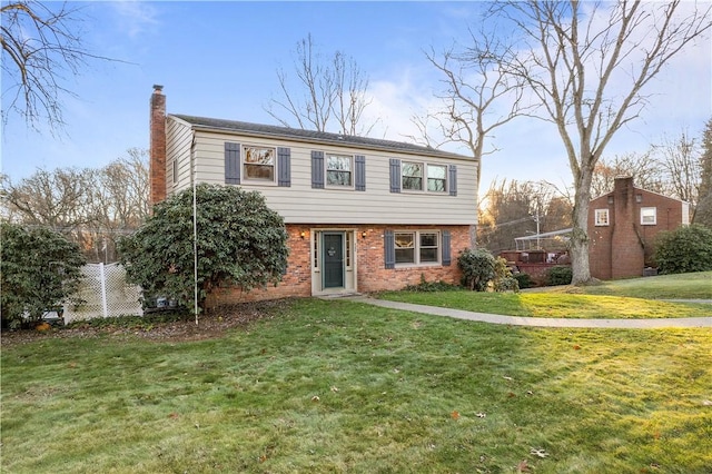 colonial house with brick siding, a chimney, and a front lawn