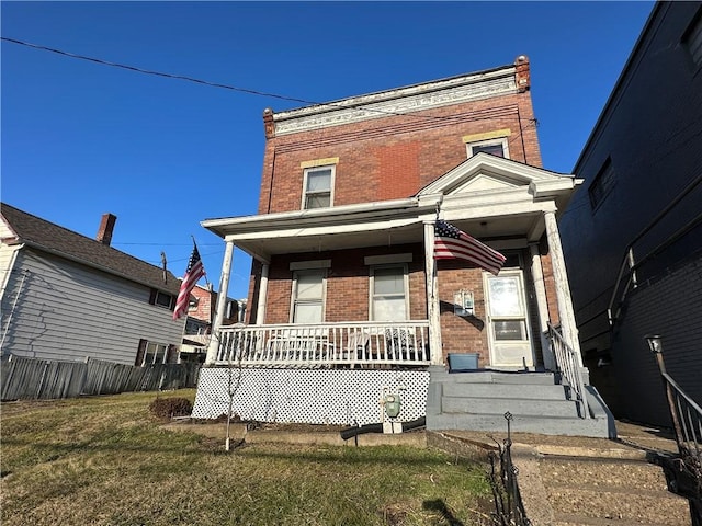 view of front of home with covered porch, brick siding, a front lawn, and fence