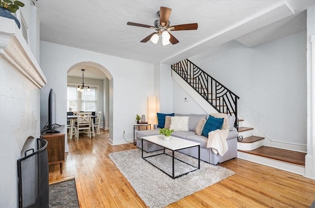 living area with arched walkways, wood-type flooring, stairway, a ceiling fan, and baseboards