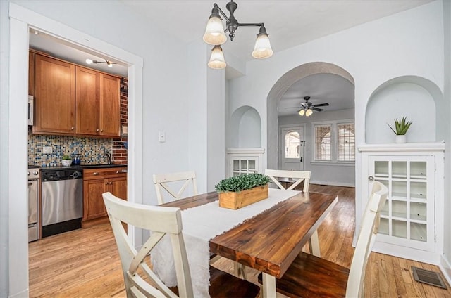 dining space with arched walkways, light wood finished floors, visible vents, and a ceiling fan