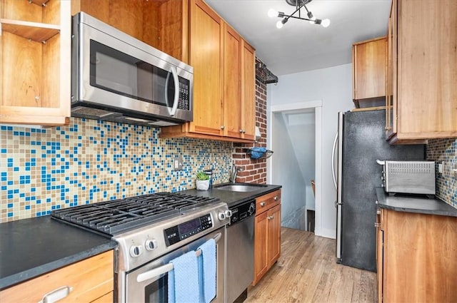 kitchen featuring decorative backsplash, dark countertops, appliances with stainless steel finishes, light wood-style floors, and a sink