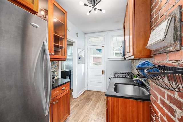 kitchen with decorative backsplash, brown cabinetry, dark countertops, freestanding refrigerator, and a sink