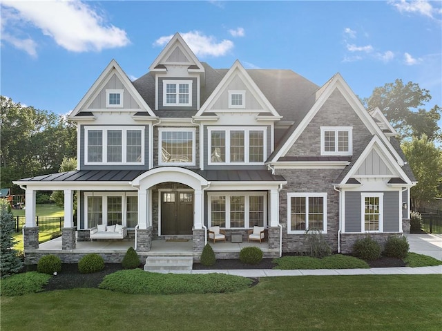 craftsman house with covered porch, a front yard, a standing seam roof, metal roof, and stone siding