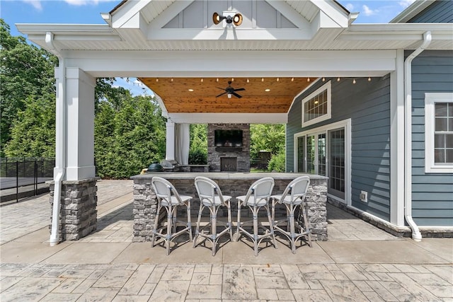 view of patio / terrace featuring an outdoor stone fireplace, outdoor dry bar, and a ceiling fan