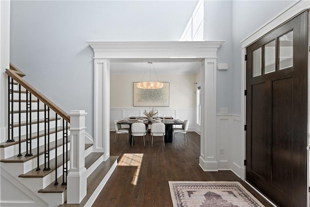 foyer entrance featuring a wainscoted wall, dark wood-style flooring, stairway, and a decorative wall