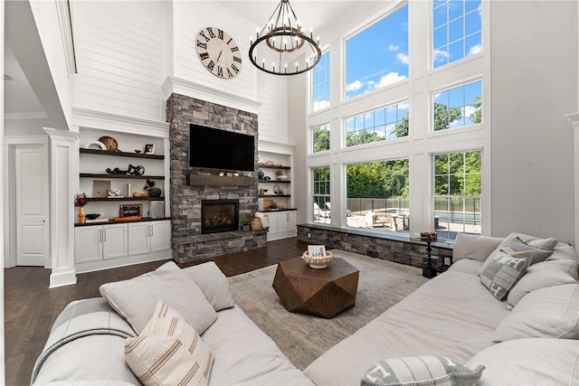 living room with a stone fireplace, dark wood-style flooring, built in features, and a healthy amount of sunlight