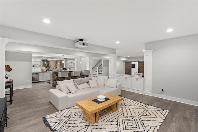 living area featuring a barn door, decorative columns, beverage cooler, stairway, and wood finished floors