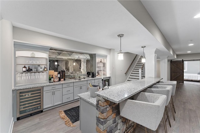 kitchen featuring a barn door, wine cooler, wood finished floors, and light stone counters