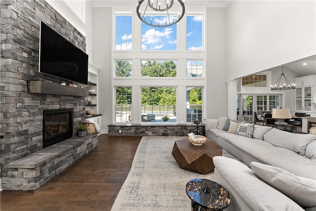 living area with plenty of natural light, a chandelier, dark wood-style flooring, and a stone fireplace