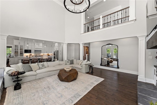 living area with dark wood finished floors, baseboards, crown molding, and ornate columns