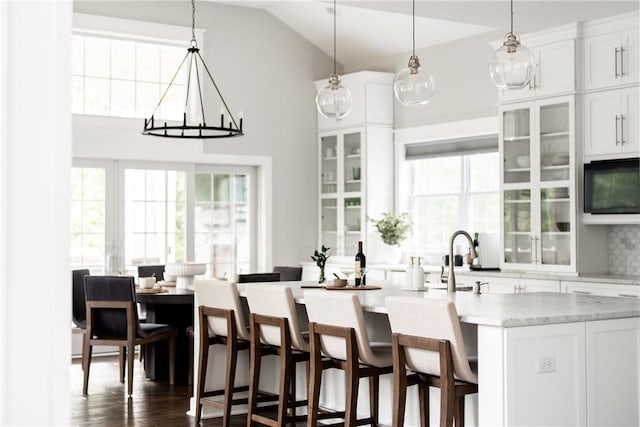 kitchen with backsplash, a center island with sink, a wealth of natural light, and white cabinetry