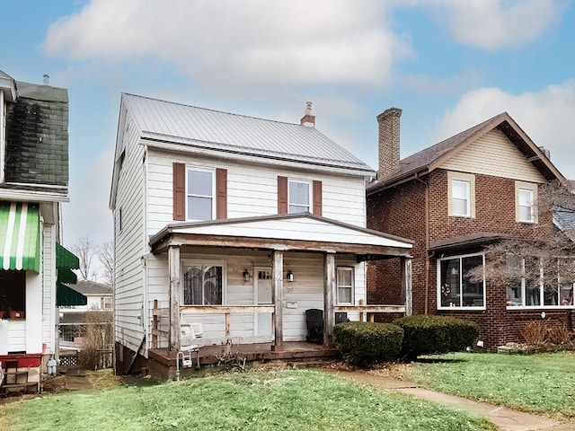 view of front of house featuring covered porch, a chimney, a front lawn, and metal roof