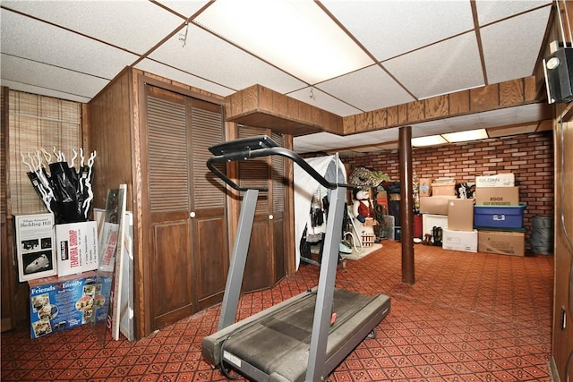 exercise room with brick wall and a drop ceiling