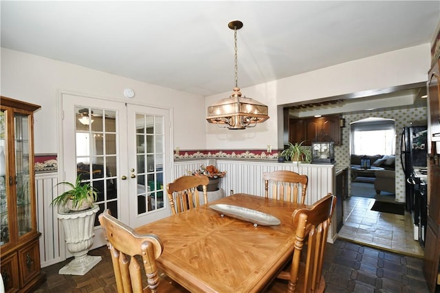 dining room featuring arched walkways, french doors, a wainscoted wall, and an inviting chandelier