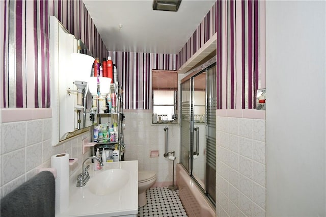 full bathroom featuring toilet, shower / bath combination with glass door, tile walls, and vanity