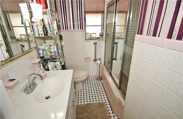 full bathroom with toilet, shower / bath combination with glass door, tile patterned flooring, vanity, and tile walls