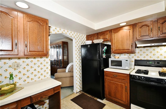 kitchen with white microwave, freestanding refrigerator, gas stove, under cabinet range hood, and wallpapered walls