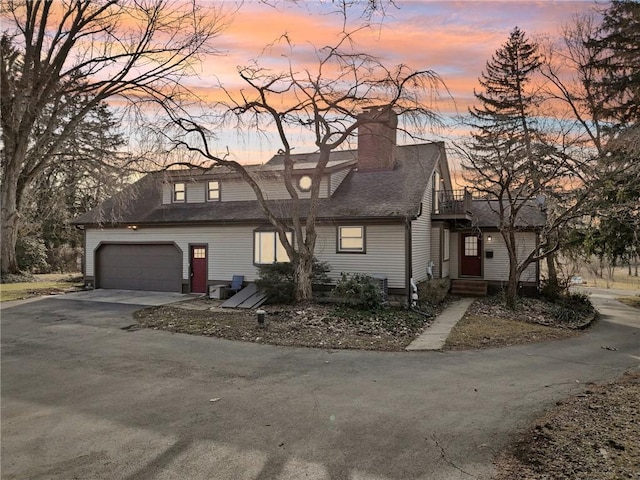 view of front of home featuring driveway, roof with shingles, a chimney, and a balcony