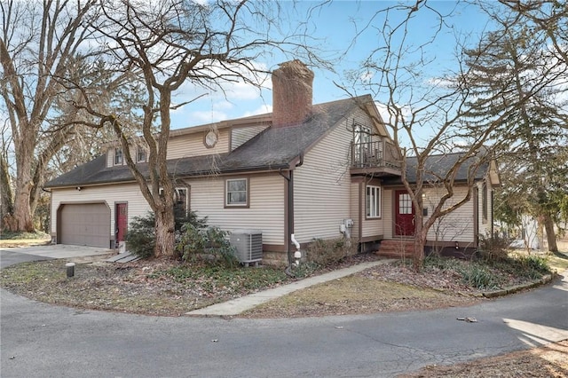 view of front of property with central AC unit, a balcony, a garage, driveway, and a chimney