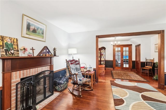 living area featuring a notable chandelier, a wainscoted wall, french doors, a brick fireplace, and hardwood / wood-style floors