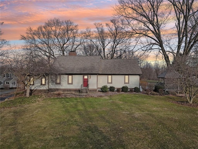 view of front facade featuring entry steps, a shingled roof, a chimney, and a front yard