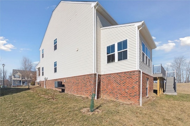 view of property exterior with brick siding, a lawn, stairway, and central AC unit