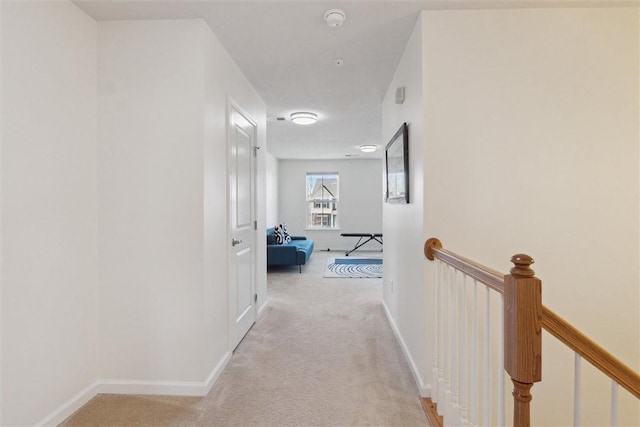 hall with an upstairs landing, baseboards, and light colored carpet