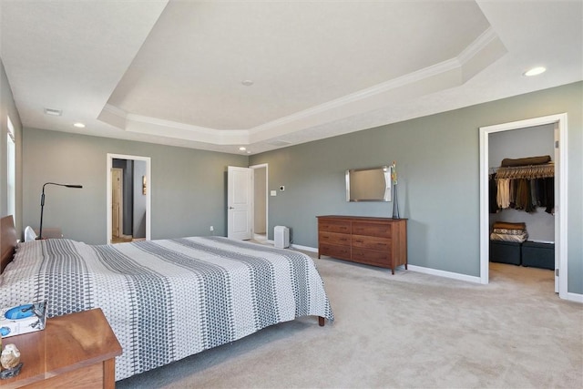 carpeted bedroom featuring recessed lighting, baseboards, ornamental molding, a tray ceiling, and a walk in closet