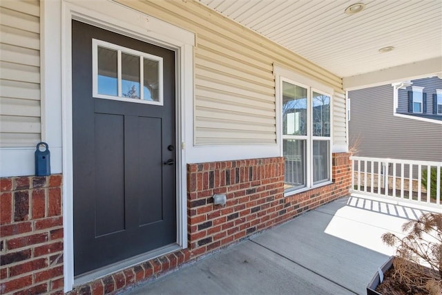 entrance to property featuring a porch and brick siding