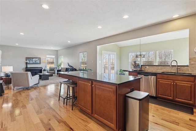 kitchen with a fireplace, a kitchen island, a sink, stainless steel dishwasher, and light wood-type flooring