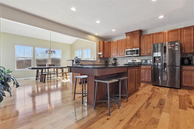 kitchen with decorative backsplash, dark countertops, appliances with stainless steel finishes, light wood-style floors, and a kitchen bar