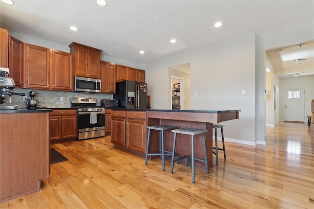 kitchen featuring light wood finished floors, stainless steel appliances, dark countertops, tasteful backsplash, and a kitchen bar