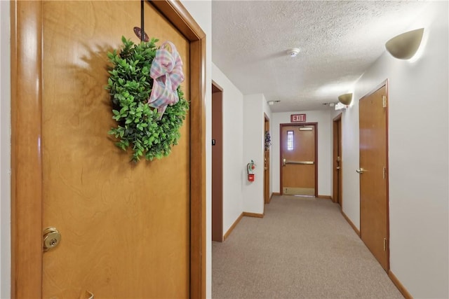 hallway with light colored carpet, a textured ceiling, and baseboards