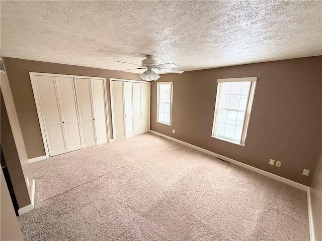 unfurnished bedroom with baseboards, carpet floors, ceiling fan, and multiple closets