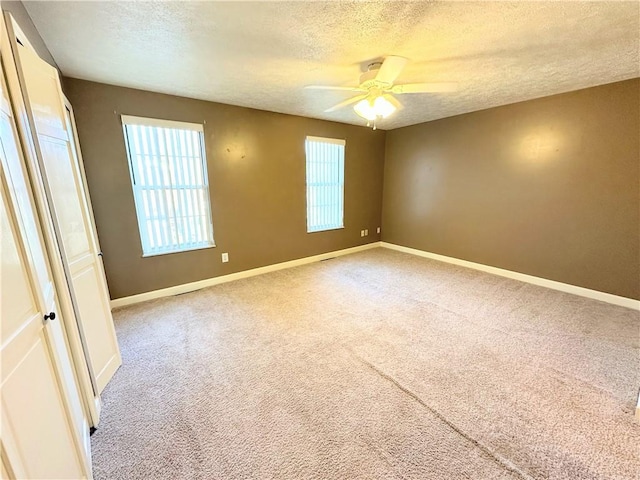 carpeted empty room featuring a ceiling fan, a textured ceiling, and baseboards