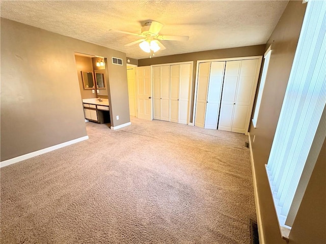 unfurnished bedroom featuring baseboards, visible vents, a textured ceiling, carpet flooring, and multiple closets