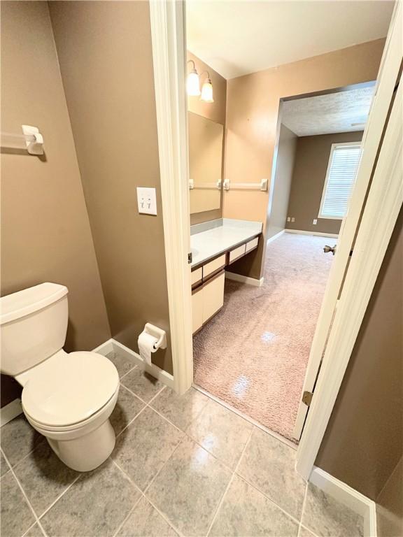 half bath with baseboards, vanity, toilet, and tile patterned floors