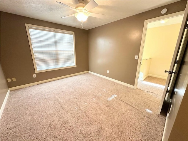 empty room featuring carpet floors, a textured ceiling, baseboards, and a ceiling fan