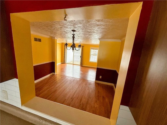 unfurnished room with a textured ceiling, a notable chandelier, wood finished floors, visible vents, and ornamental molding