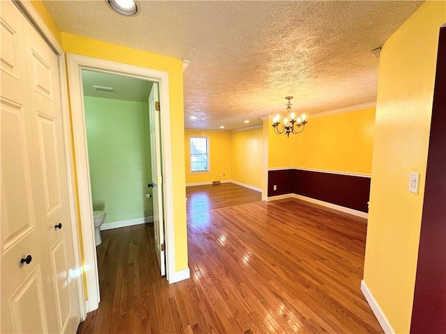 empty room with a notable chandelier, visible vents, baseboards, and hardwood / wood-style floors