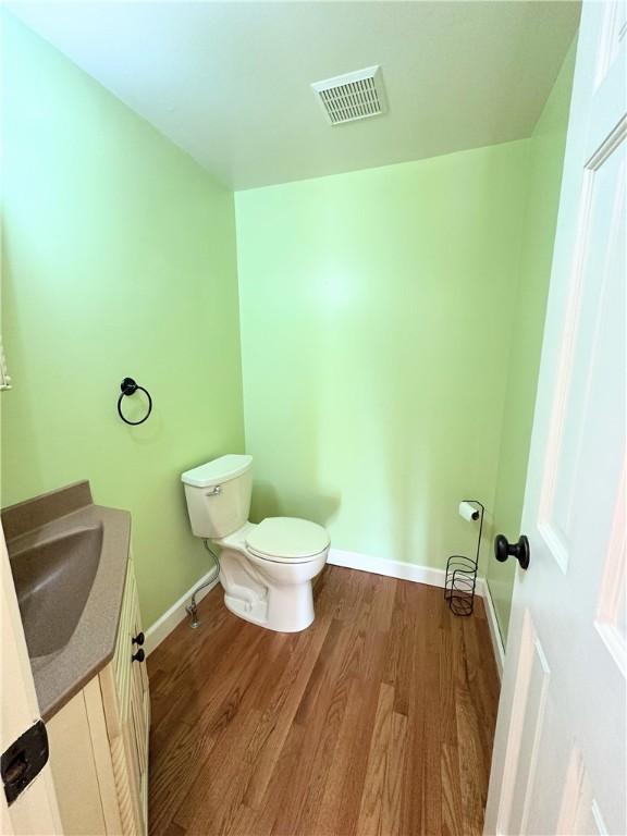 half bathroom with baseboards, visible vents, toilet, wood finished floors, and vanity