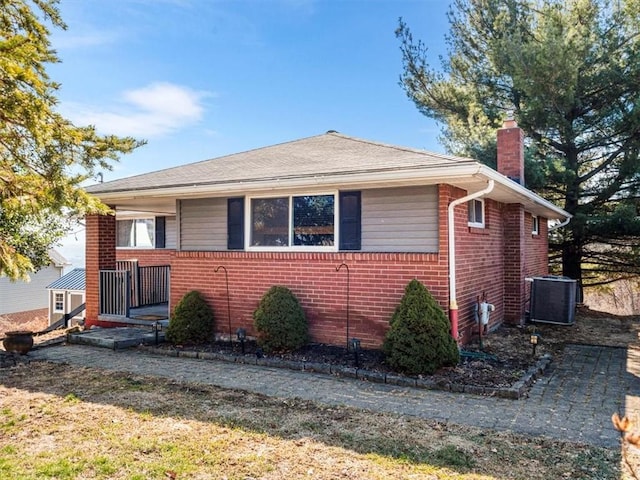 view of front of house featuring brick siding, a chimney, and central air condition unit